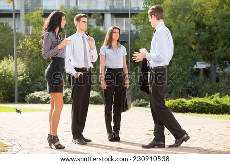 Group of young business people standing in a park near their company on the coffee break, talking to each other, enjoying the beautiful day.
