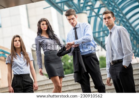 Small group of business people, formally dressed, standing on the steps of the office building as if expecting someone, while a young businessman looking at his watch in his hand.