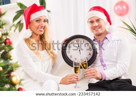 Happy beautiful couple Celebrating New Year in home interior and showing midnight on the clock.