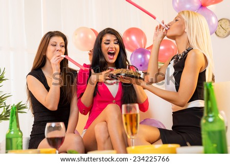 Two young attractive girls, elegantly dressed, prepared surprise their friends, giving her a birthday cake, playing in the party whistles.