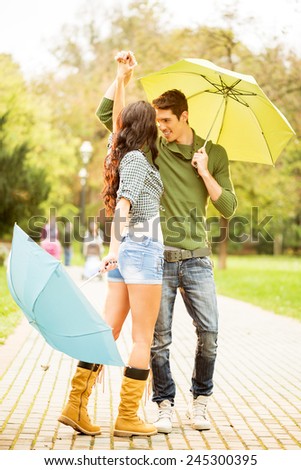 Young couple in love, dancing in the park with umbrellas in hands.
