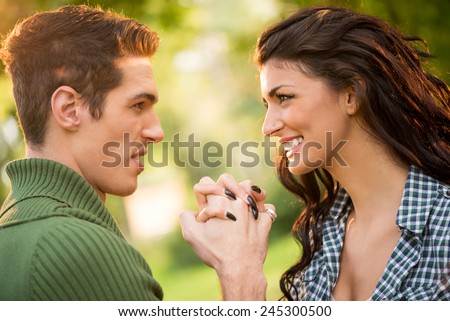 Close-up of a young heterosexual couple, holding hands facing each other and look at each other with a smile.