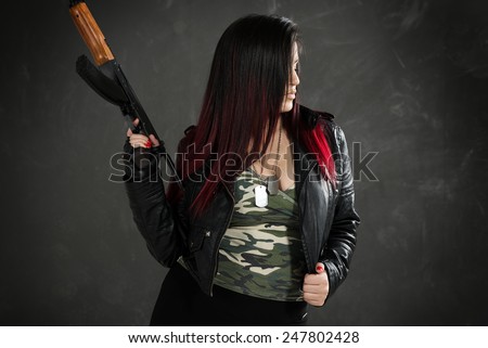 Profile of an attractive young woman in a leather jacket and camouflage shirt with cleavage with a Kalashnikov in her hand.
