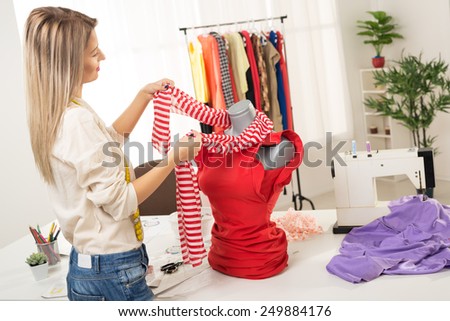 Young woman, fashion designer, creates a dress on mannequin. In addition to the mannequin on the table is sewing machine.