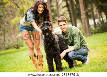 Young pretty brunette caresses a dog, a large black schnauzer. Beside a dog crouching handsome guy with a smile looking at the camera
