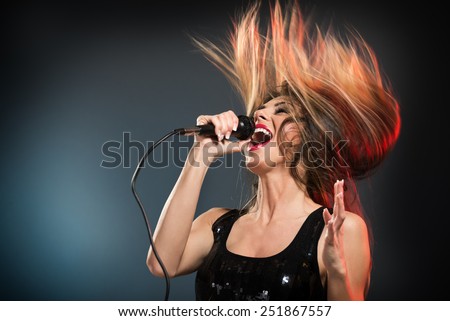 A young woman rock singer with tousled long hair holding a microphone with stand and sing with a wide open mouth.