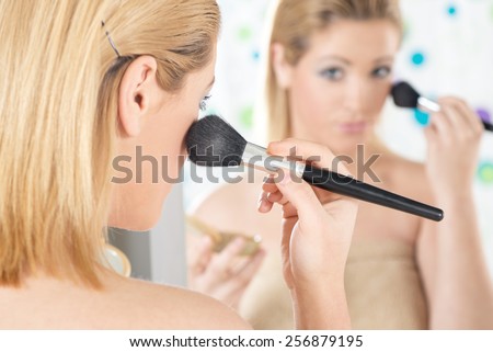 Close-up of beautiful girl with blue eyes applying blush in front of mirror in his bathroom in the morning. Rear view.