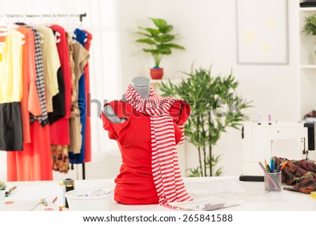Dress on mannequin in fashion designer office. In addition to the mannequin on the table is sewing machine. In the background you can see hanging garments.