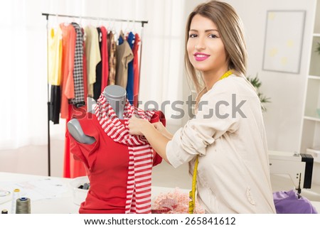Young woman, fashion designer, creates a dress on mannequin. Looking at camera.