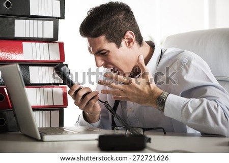 Young Angry Businessman sitting in the office and screaming on the phone.