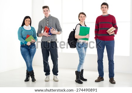 Group of cheerful students with book\'s standing in school hall and looking at camera.