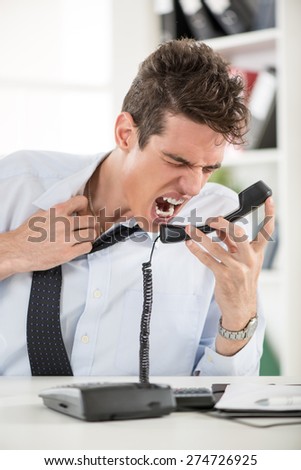 Angry young Businessman sitting in the office and screaming on the phone