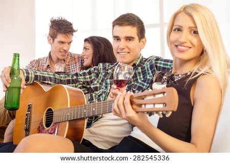 Small group of happy young people hang out at the house party with an acoustic guitar.