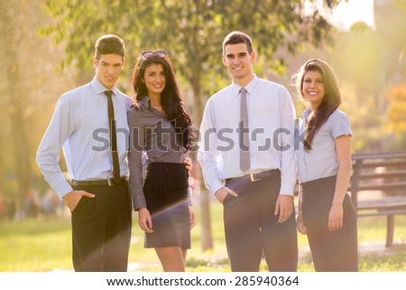 Small group of business people, elegantly dressed, standing in the park, looking at the camera, enjoying the sunny day.