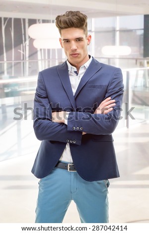 Serious young businessman standing in the lobby of the company with crossed arms. Looking at camera.