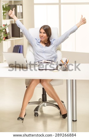 Young pretty businesswoman in the office sitting in office chair with thumb up.