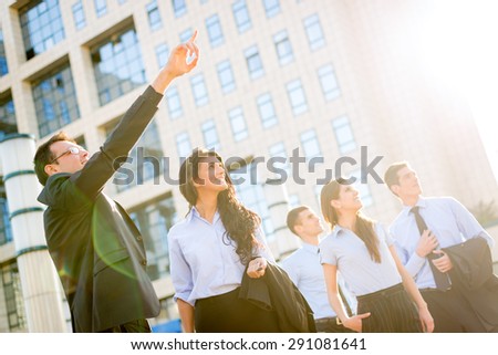 The young businessman in front of office building outstretched fingers of the hand, aimed at heights, shows his young business team motivating them to new business success.