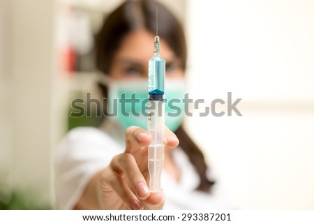 Close-up injections with blue liquid, in the hands of a nurse with a face out of focus.