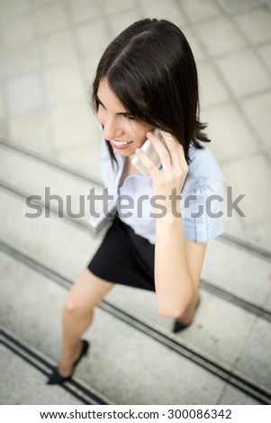 Young beautiful business woman coming on stairs in front of office building and talking on mobile phone.