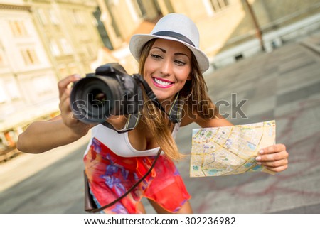 Beautiful young girl tourist holding map and photographed with digital camera.