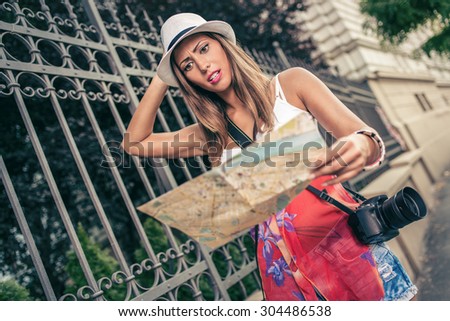 Beautiful woman on vacation walking on the city and worried studying map of city. She is holding a digital camera.