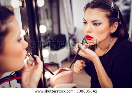 Portrait on mirror of a beautiful pin-up girl applying red lipstick to her lips. Close up.