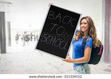 Happy beautiful teenage girl with school bag holding a sign \'Back to School\'. Looking at camera.