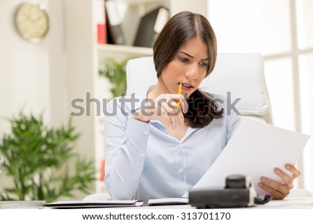Portrait of a beautiful young businesswoman sitting in the office, biting pen and thinking.