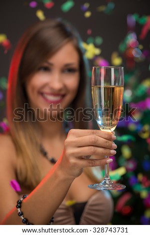 Close-up of a beautiful woman holding with champagne. Focus on foreground, on champagne. Confetti is the air.