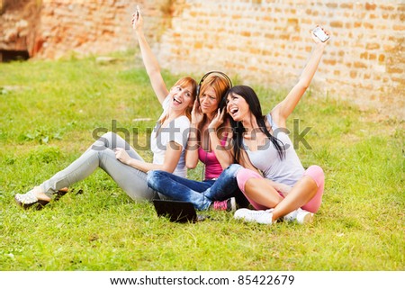 Three young beautiful girls listen music from notebook outdoor