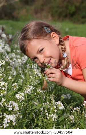 Pretty young girl leaning over to smell flowers in a field