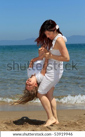 Mother playing with her daughter and holding her upside down on a beach