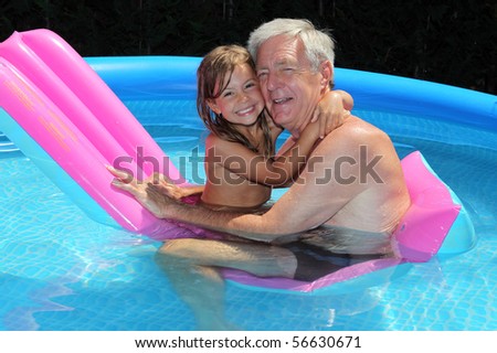 Grandfather and granddaughter cuddling on a lilo in a swimming pool
