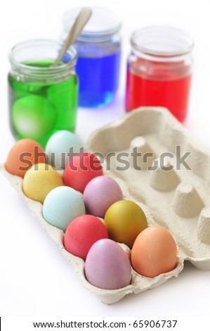 Colorful Easter eggs in the egg carton and glass jars with dye on the background