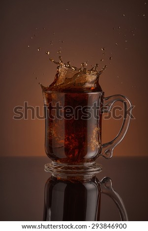 Refreshing splash of black ice coffee drink on a brown background. Liquid drink pouring into a cup with ice. Pour high speed beverage for promoting restaurant, bistro and bar. Close-up design liquor