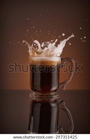 Splash of  ice coffee drink on a brown background. Refreshing Iced cappuccino liquid drink pouring into a mug, cup with ice cubes. Cold beverage wave. Close-up design liquor milk, coffee and ice.