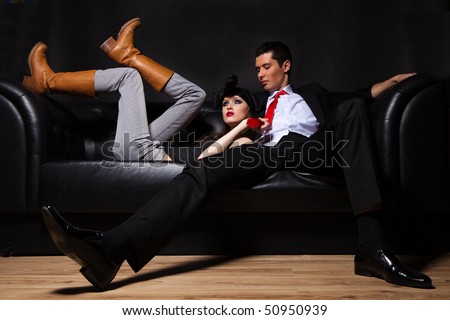 Young glamorous loving couple on black sofa.
