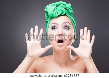 Surprised excited woman with pink-green makeup in green hat with open mouth
