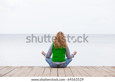 Yoga woman sitting back on wooden bridge near the ocean