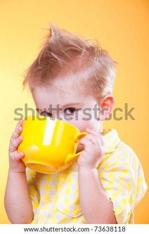 Portrait of funny little boy drink from big yellow cup