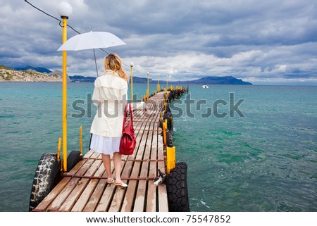 Woman walking on sea footbridge walking with umbrella and bag
