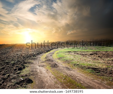 Country road through the plowed land at sunset