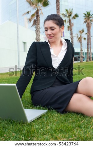 Business woman in black suit with a laptop sitting on the grass