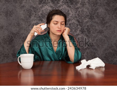 Woman suffering from headache and flu symptoms at home with a coffee cup and tissues taking her temperature