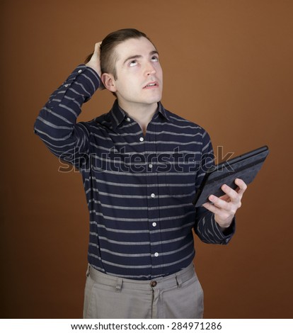 Nice shot of a young man using a tablet reacting to the content in a casual outfit on a brown background with room for copy