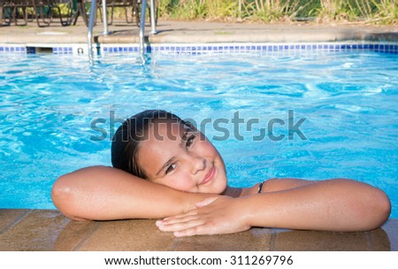 Tween girl in a pool peeking over the edge looking right at the camera with big eyes