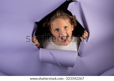 Studio shot of a silly girl with glitter in her hair breaking through purple paper with a crazy look and silly hair.