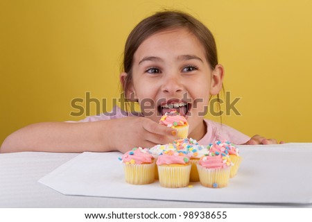 Young girl eating cupcakes with big brown eyes on a yellow background