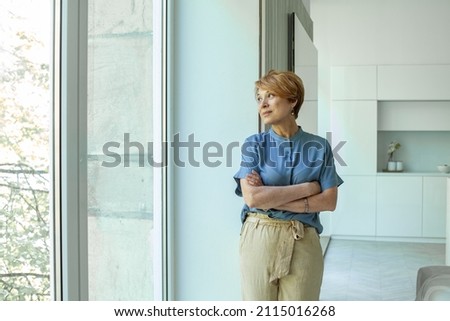 Middle aged lady in casual clothing standing near window at home Stock fotó © 