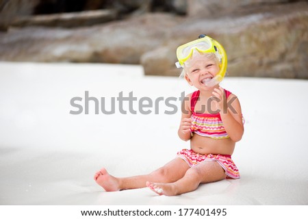 Cute little girl wearing mask and snorkel on white tropical beach